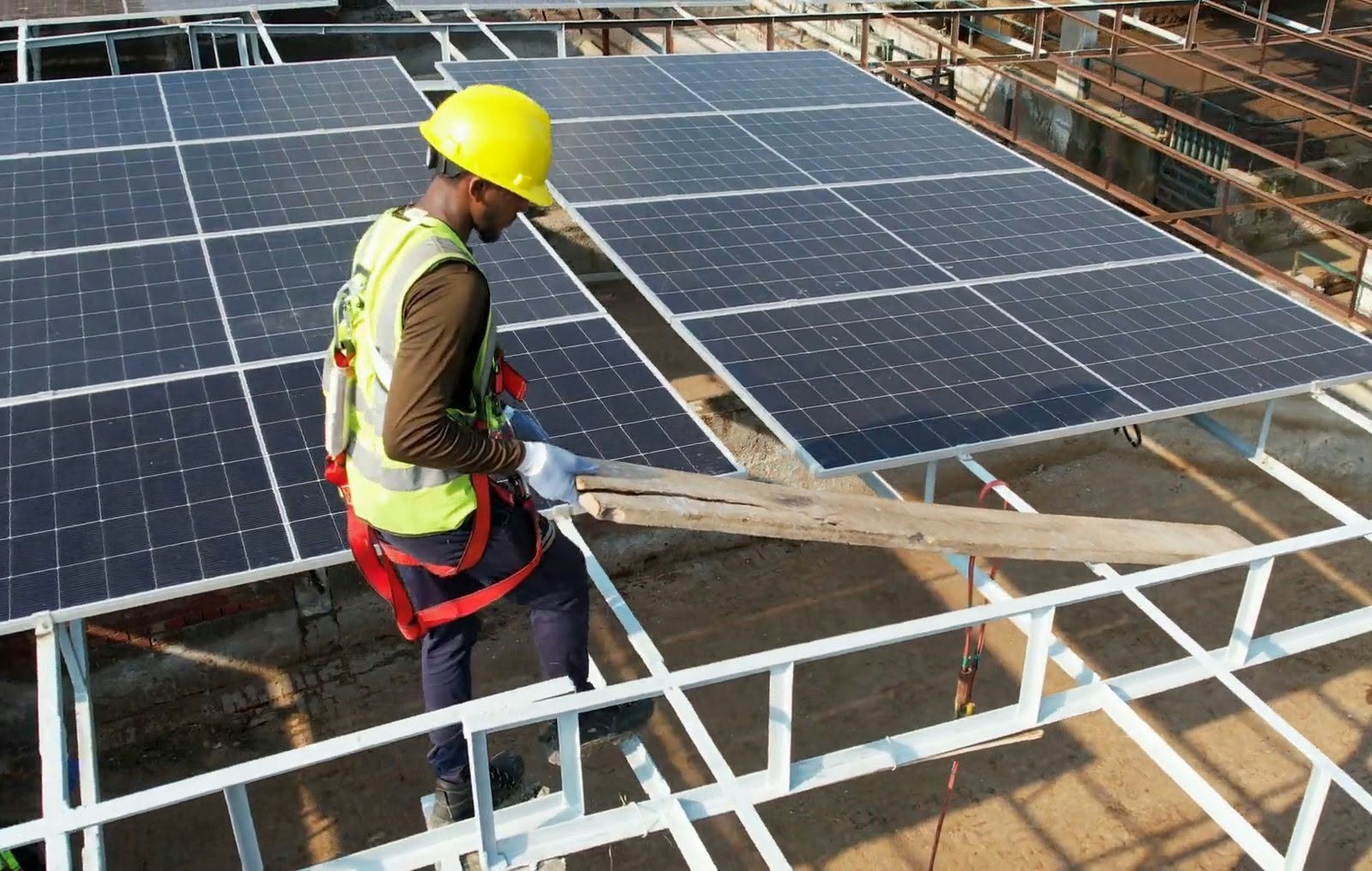Tekton solar installer in a helmet and harness working on the panel mounting frame